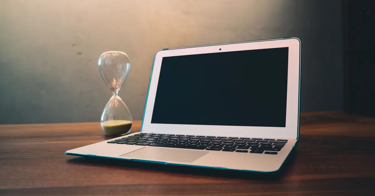 An hourglass beside a laptop on a wooden desk, standing in for the time payback of a plugin
