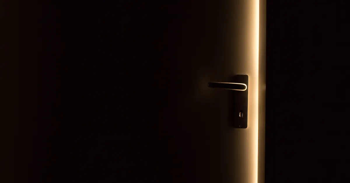 The handle of a half-open door in a dark room, with light along the door's edge